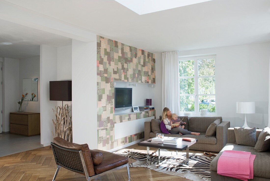 Moderne Sitzgruppe mit Zebrafellteppich vor einer im Patchworkmuster gestalteten Medienwand im offenen Wohnraum; Mutter sitzt mit Kleinkind auf Sofa