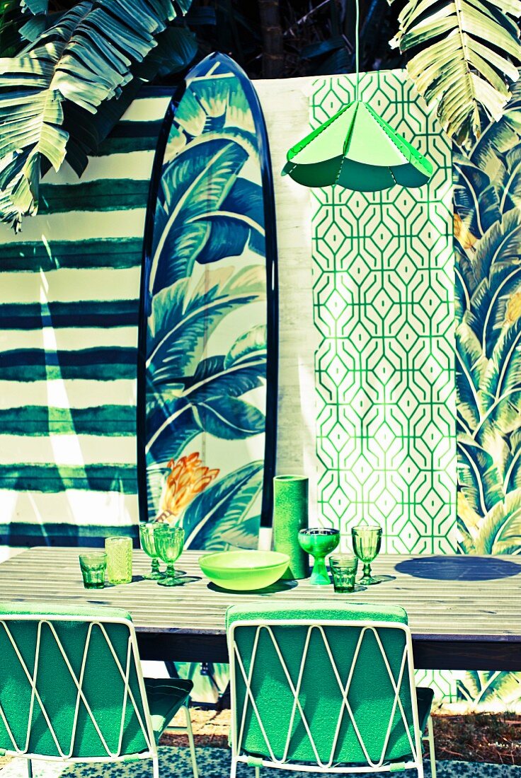 Tapetenstreifen mit grünem Mustermix als Hintergrundkulisse und mit passenden Accessoires dekorierter Essplatz im Freien