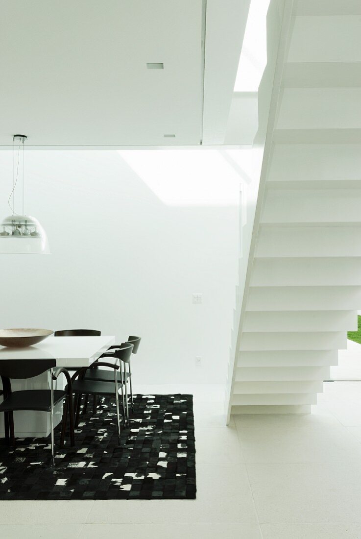 Black and white designer dining area next to bottom view of white, free-standing staircase