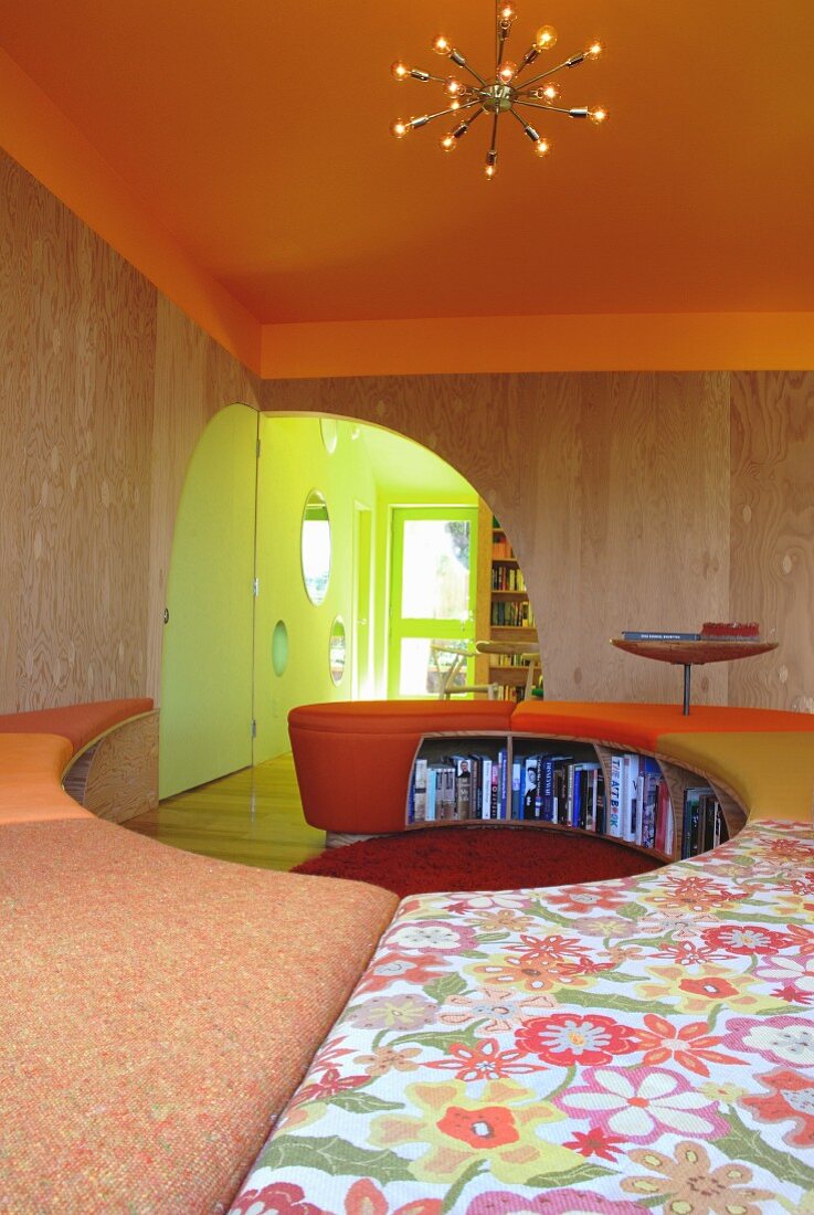 Curved bench with colourful seat cushions and orange-painted ceiling with sunburst pendant lamp; quarter-circular doorway in background