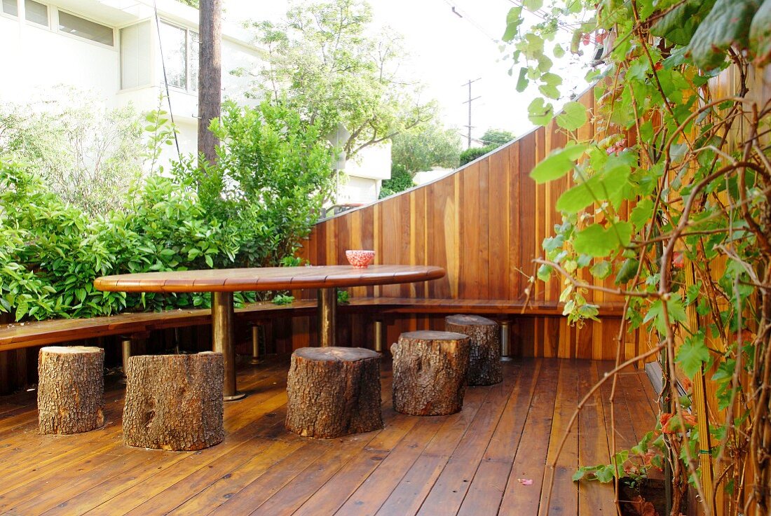 Holzterrasse mit selbstgebauten Sitzhockern aus Baumstämmen und Tisch in städtischem Umfeld