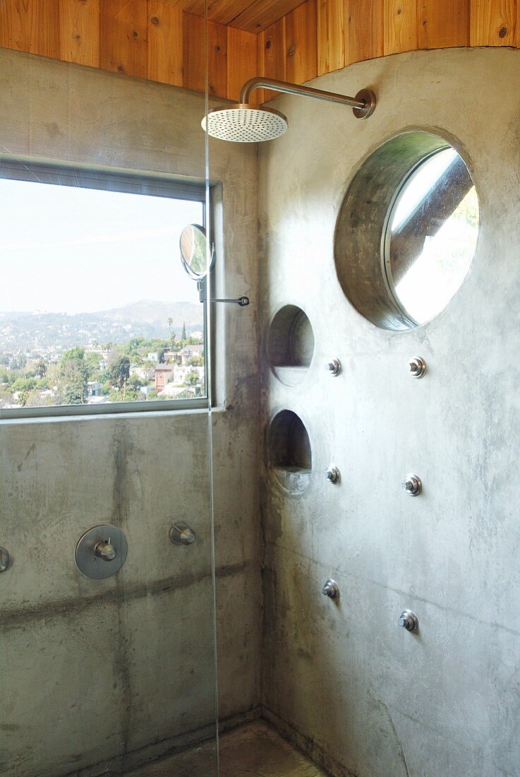 Shower in front of window with view in corner of bathroom with concrete wall panels and round recessed shelves