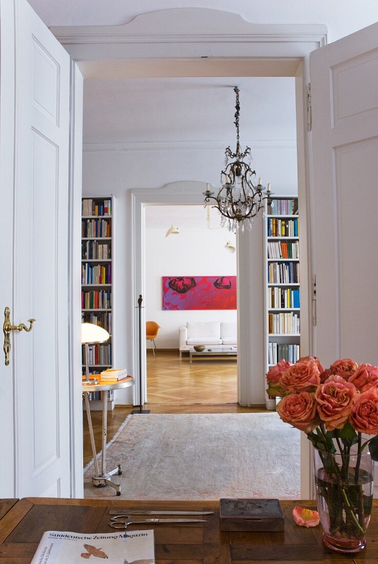 Vase of roses on desk in front of open double doors with view through library into living room of period apartment