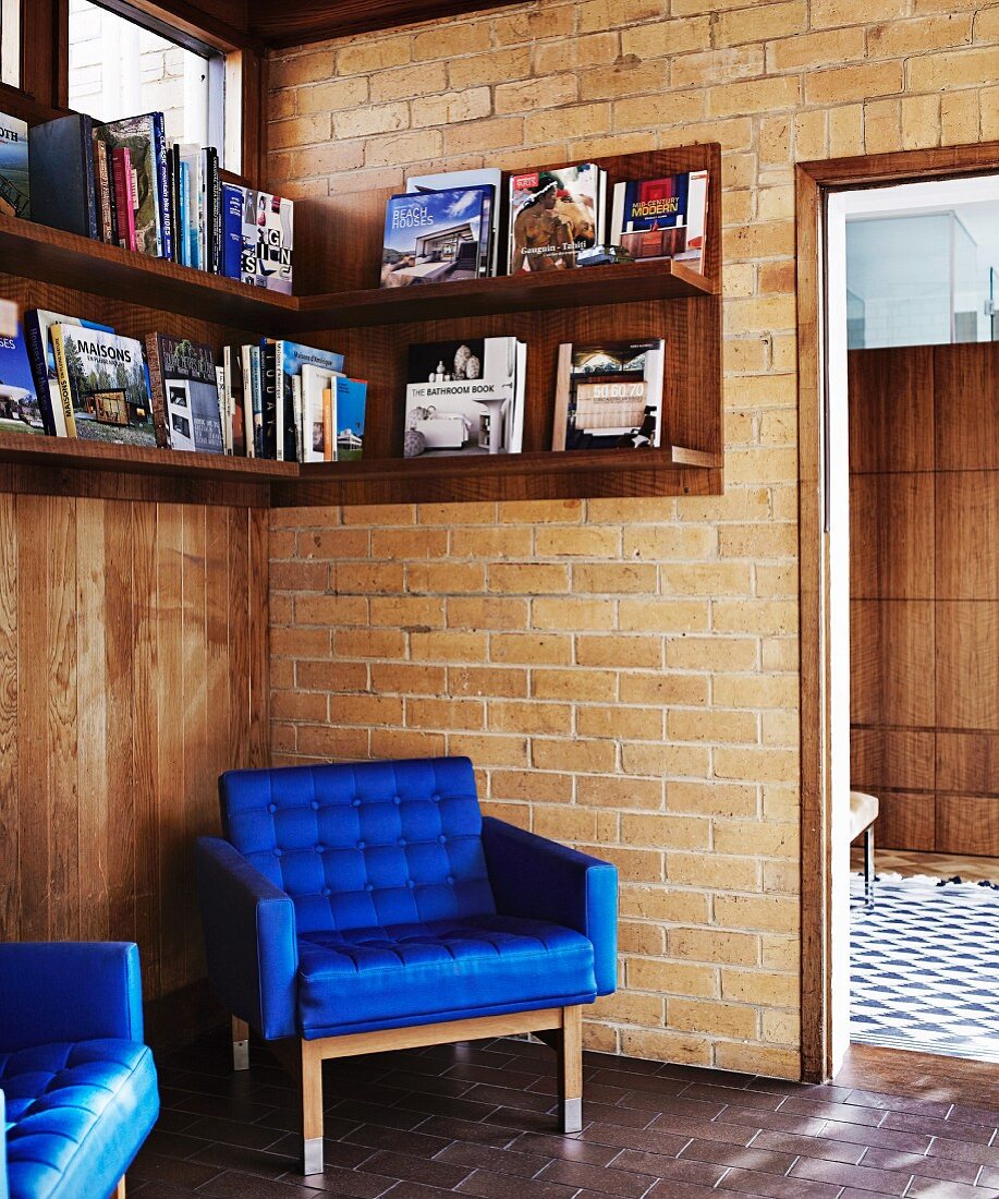 Sessel mit königsblauem Bezug unter Bücherbord an Ziegelwand in Zimmerecke