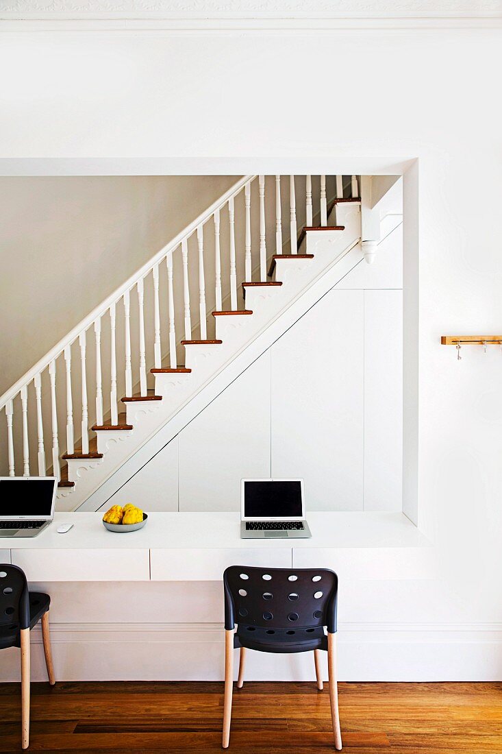 Wandausschnitt mit integrierter Schreibtischplatte, Laptops und modernen Stühlen; Blick zum Treppenaufgang