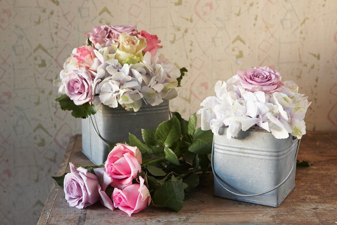 Romantische Rosengestecke in Zinkeimerchen und Rosen auf Holztisch; Vintage Ambiente