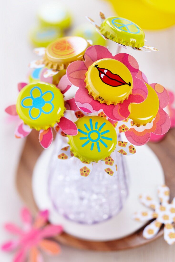 Bottle caps painted yellow with various motifs used as funky centres of pastel paper flowers