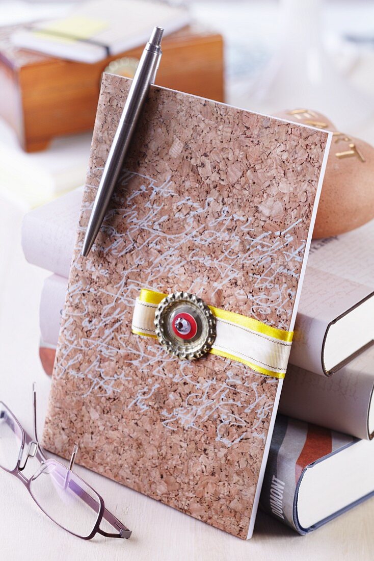Elegant cork envelope decorated with ribbon and flattened bottle cap leaning against stack of books