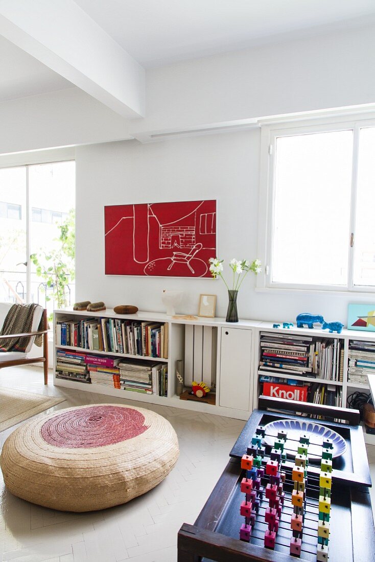 Three-dimensional game on tea trolley, two-tone floor cushion and half-height bookcase against wall in minimalist, loft-style interior