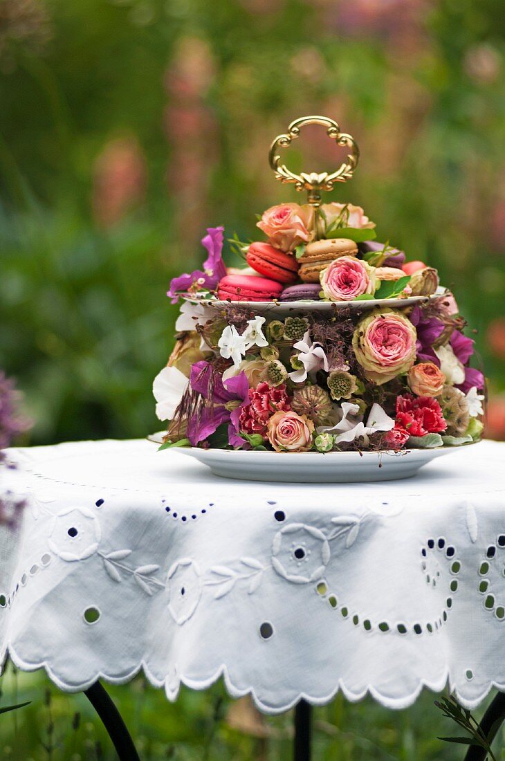 Festively decorated cake stand decorated with roses and other flowers on white broderie anglaise tablecloth in summery garden