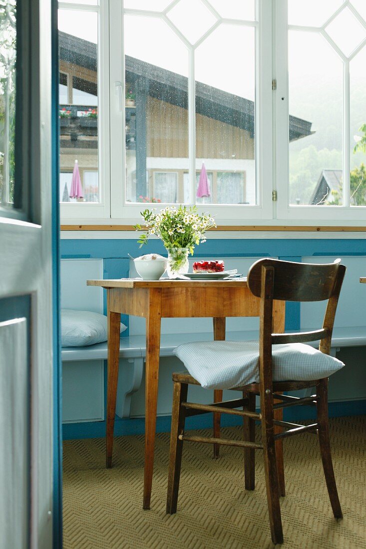 Cosy restaurant with set coffee table and pale blue bench below window in renovated country house
