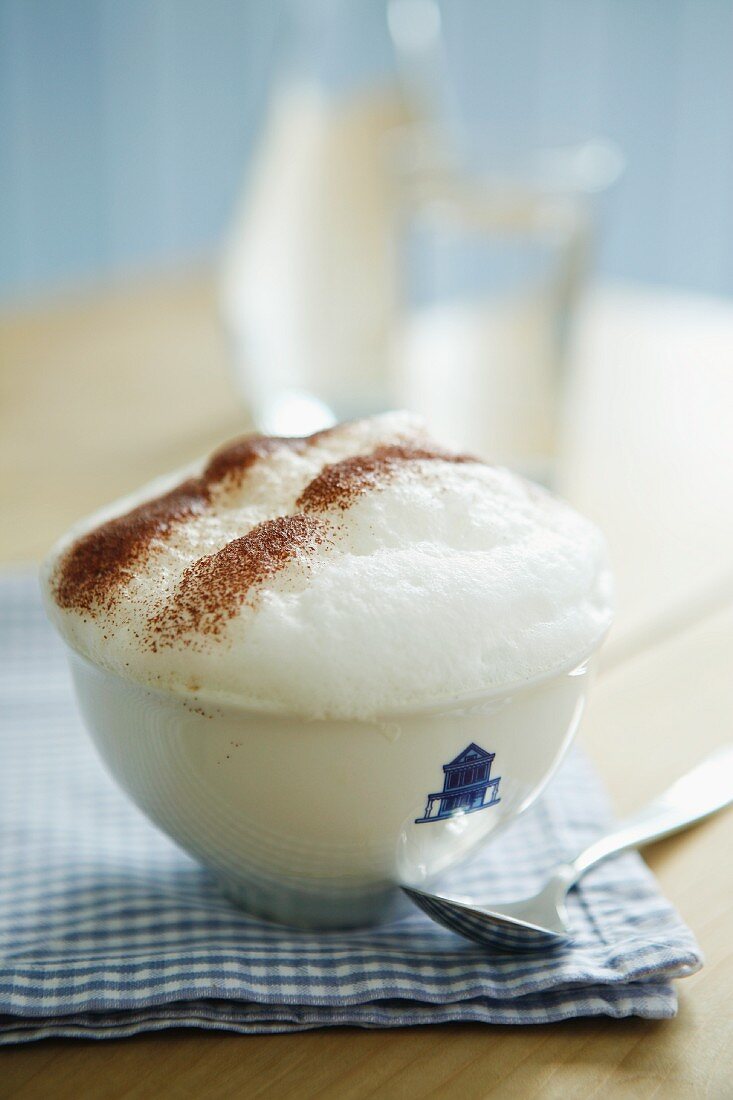 Eine Tasse Cappuccino mit Milchschaum auf blau-weiß karierter Serviette im Landhausstil