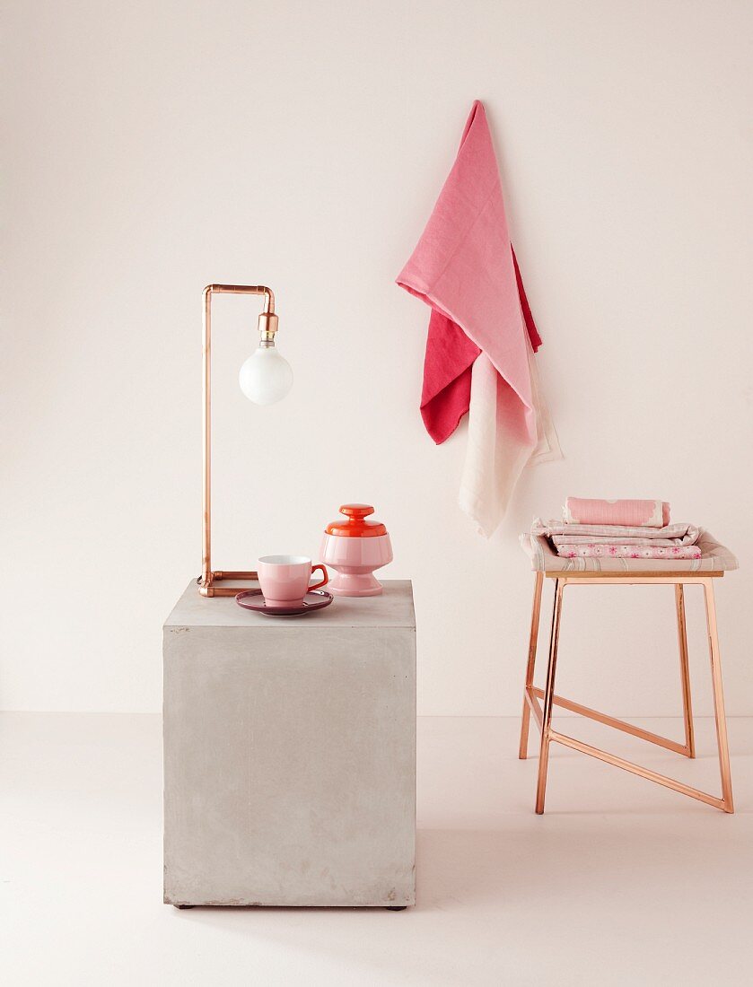 Purist lamp made from angled copper pipes and copper stool; crockery and fabrics in shades of pink