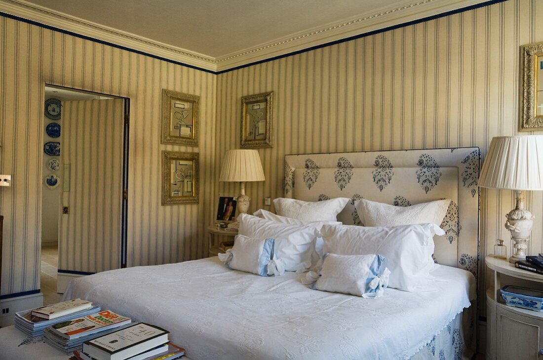 Bedroom in classic, English style with elegant, striped wallpaper, upholstered headboard and scatter cushions on double bed