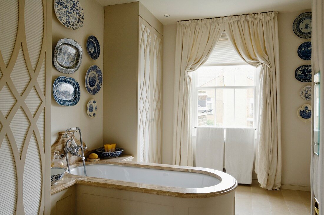 Collection of decorative plates above wood-clad bathtub with marble edge in stylish, English bathroom
