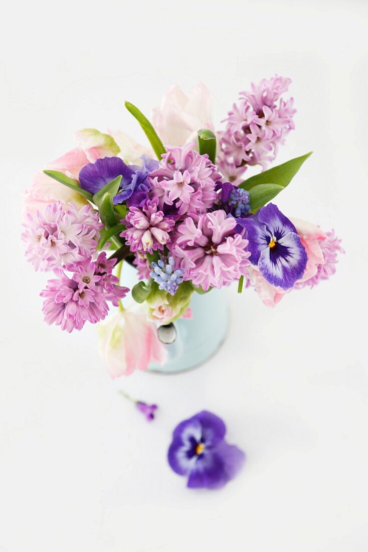 Frühlingsstrauss in Pastelltönen aus Hyazinthen, Tulpen und Stiefmütterchen in hellblauer emaillierter Kanne