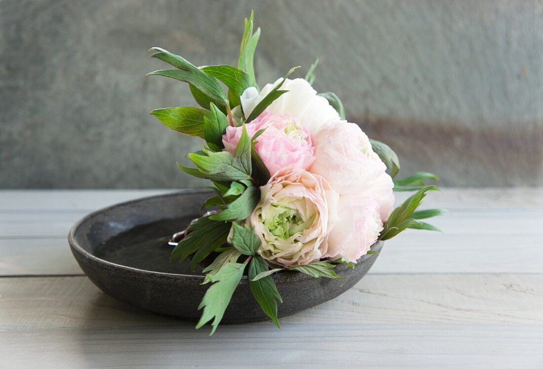 Peonies in dish on wooden surface