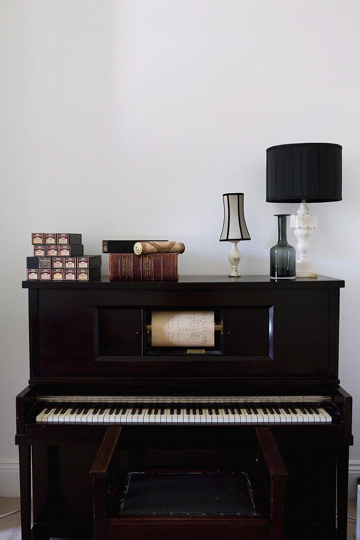 Schachteln, ein antiquarisches Buch und Tischleuchten auf Pianola mit Notenrolle