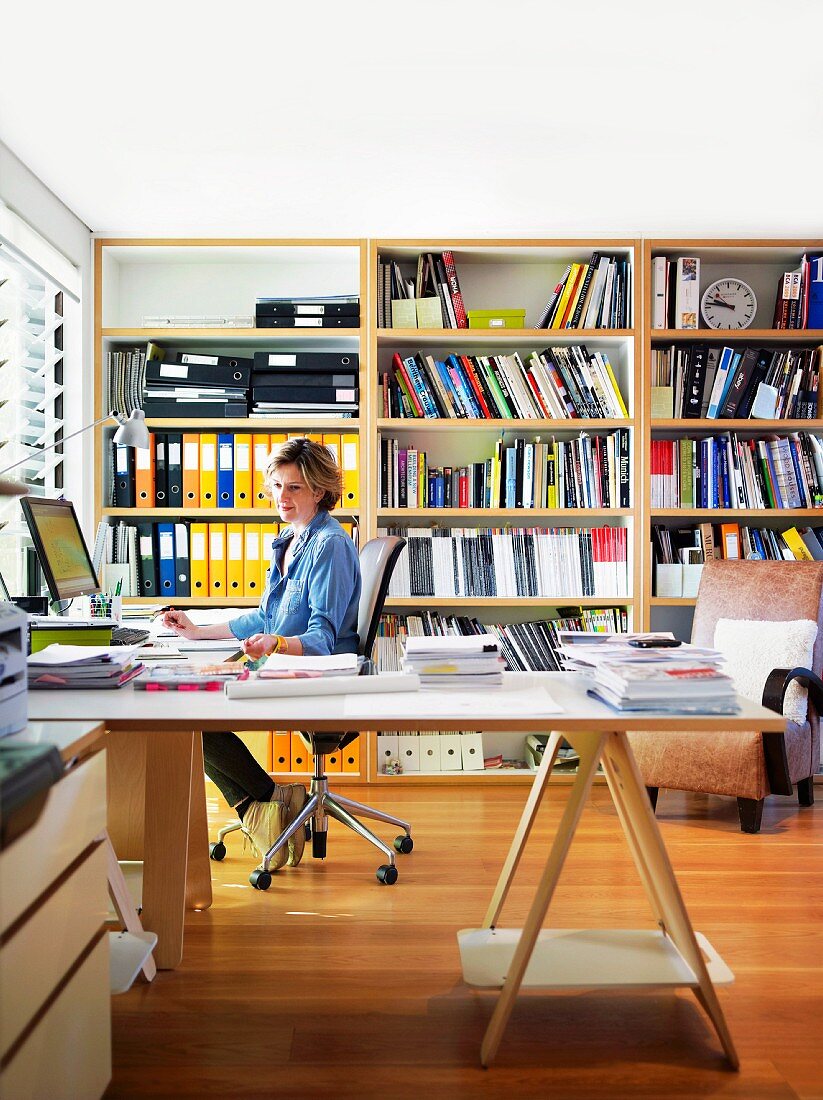 Frau an grossem Übereck-Schreibtisch in Homeoffice, im Hintergrund Bücherregal