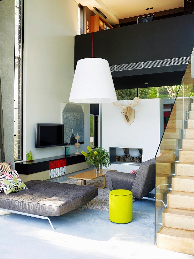 Designer sofa in open-plan, double-height living area with stairs leading to gallery bridge