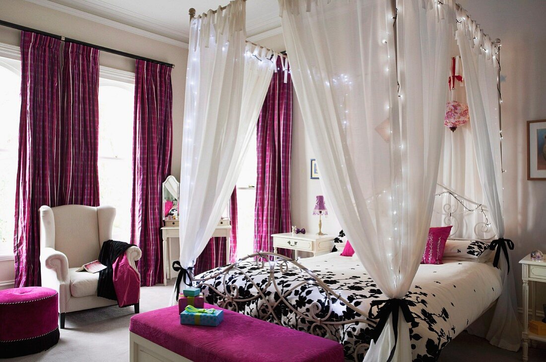 Four-poster bed decorated with fairy lights and purple textiles in elegant bedroom