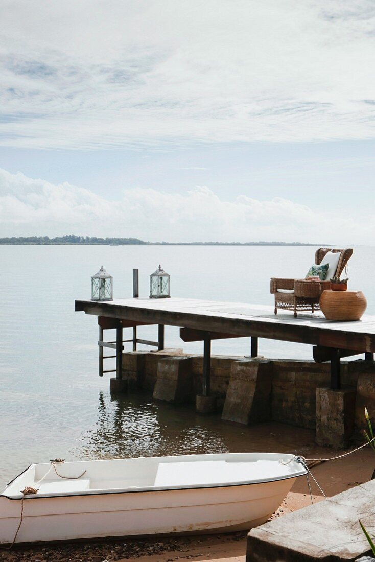 Stimmungsvoller Sitzplatz mit Laternen auf Bootssteg am Meer, im Vordergrund weisses Boot an Ufer