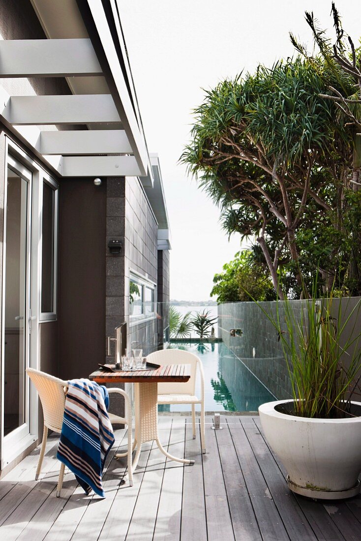 Striped blanket on chair at table opposite white planter of ornamental grasses on wooden terrace