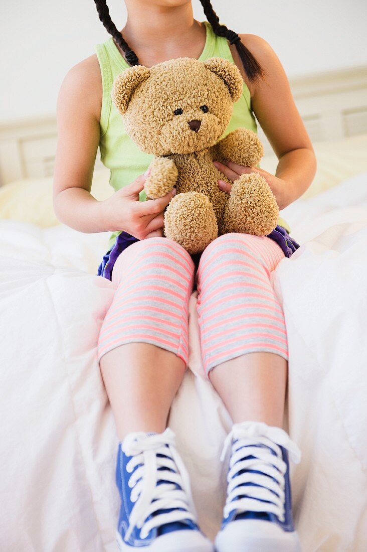 Mädchen hält Teddybär auf dem Bett