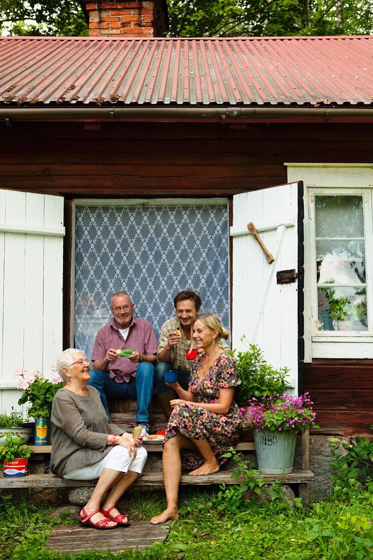 Rustikales Wochenendhäuschen - Famile auf Holzstufen vor offener Tür mit geschlossenem Vorhang