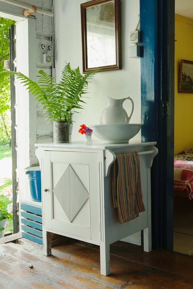 weiße Waschschüssel und Krug auf halbhohem, weißem Schrank an Wand, zwischen offener Haustür und Zimmertür