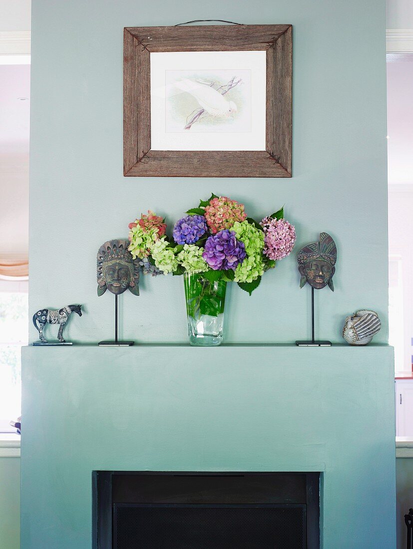 Open fireplace painted pale grey as partition; bouquet and ethnic masks on mantelpiece