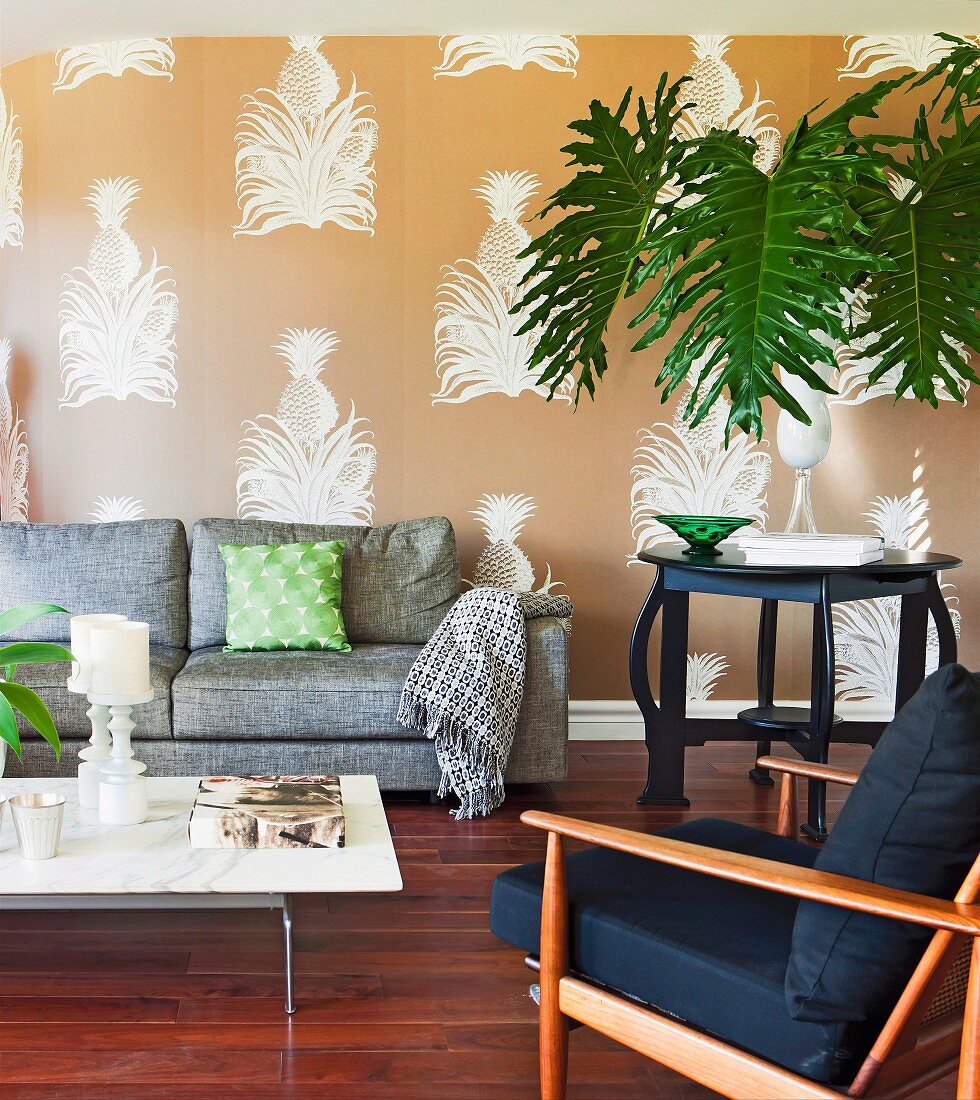 Wohnzimmer mit 50er Jahre Sessel, modernem Sofa und goldfarbener Tapete mit Ananas-Motiven