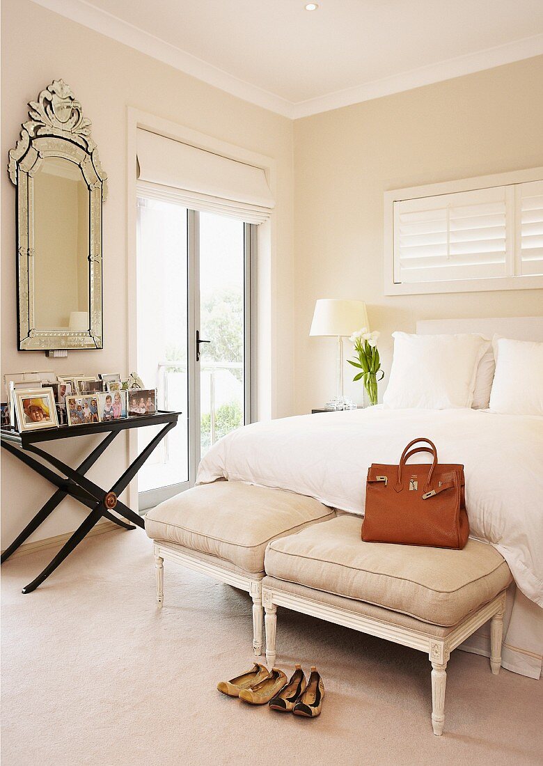 Bank im Rokoko Stil mit Polstern und Ledertasche am Bettende eines Doppelbettes und Wandtisch mit Spiegel in hellem Schlafzimmer