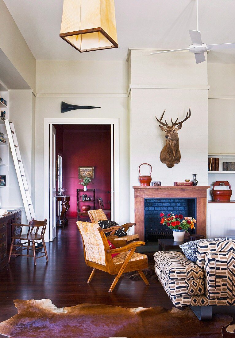 Living room with rustic ambiance; 50s-style armchairs in front of open fireplace below hunting trophy