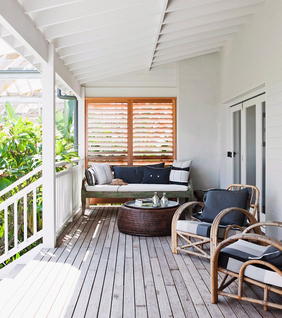 Rattan armchairs and coffee table on roofed wooden veranda adjoining house