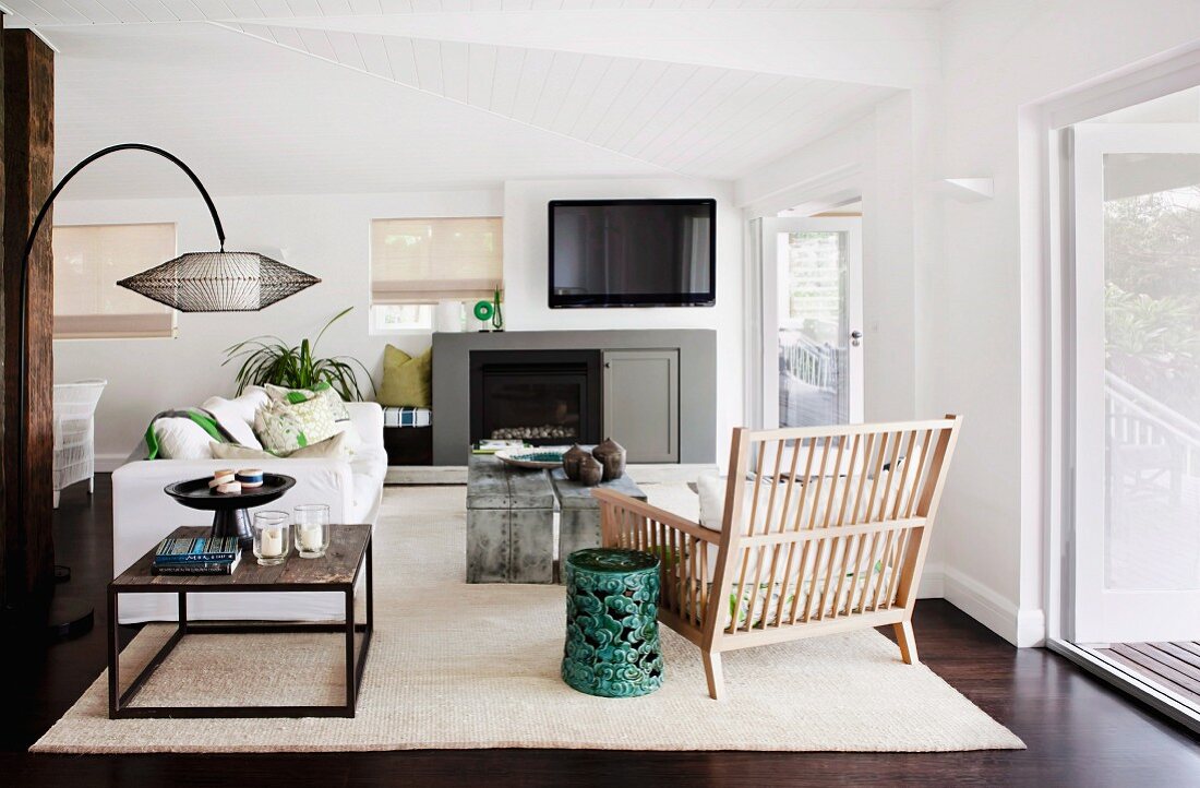 Modernes Wohnzimmer mit Couchtisch und rustikalem Sessel aus Holzlamellen vor Kamin & Fernseher