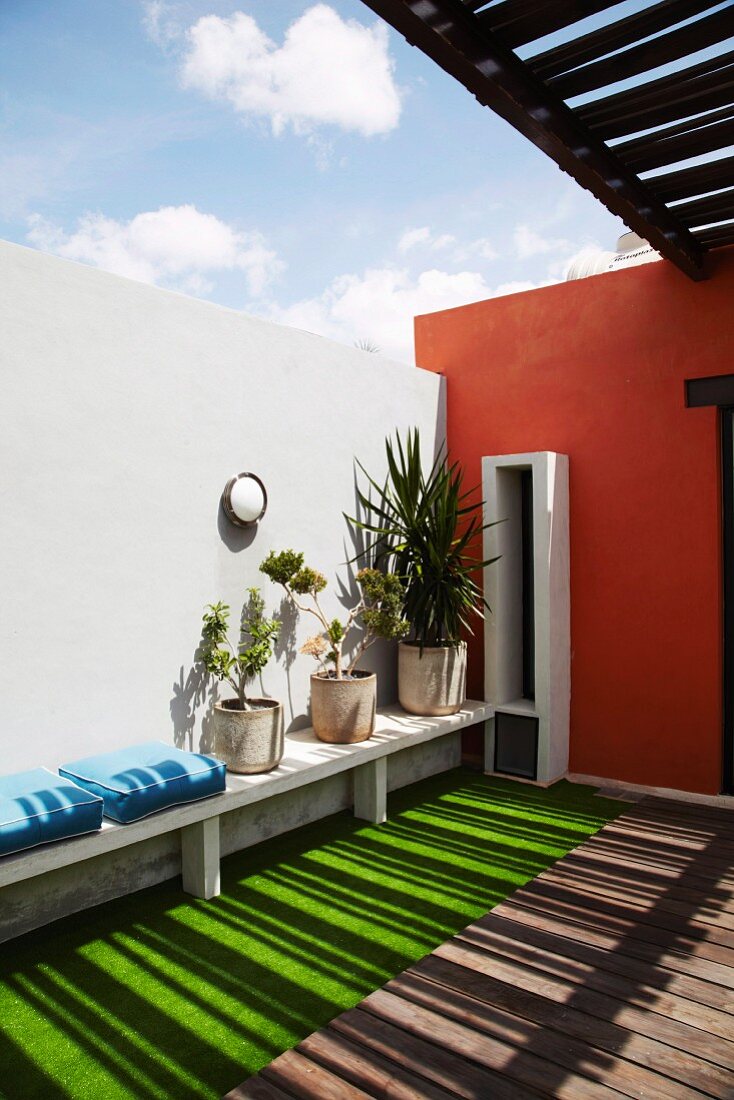 Licht- und Schattenspiel auf geschützter Terrasse mit grünem Boden und weiss hervorgehobenem Fensterschlitz in ziegelroter Wand