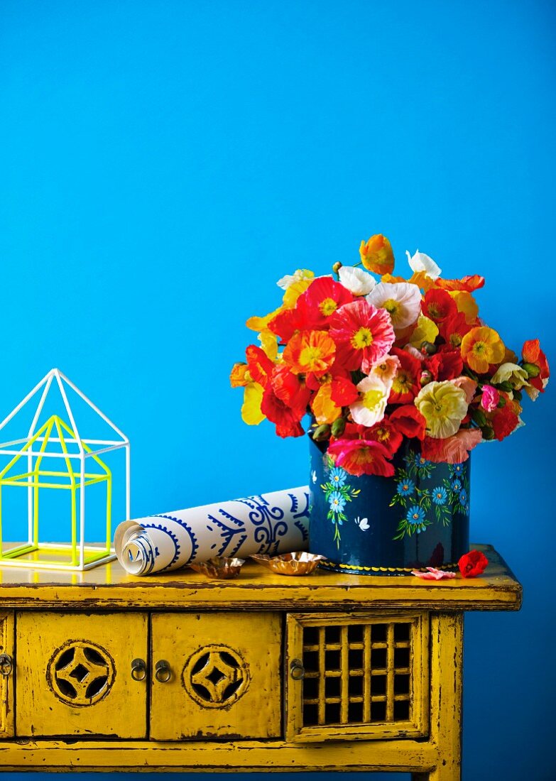 Bunter Blumenstrauss und Tapetenrolle auf Vintage-Kommode vor blauer Wand