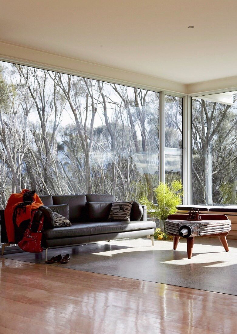 Modernes Sofa und rustikaler Beistelltisch in rundum verglastem Wohnraum mit Blick auf Bäume