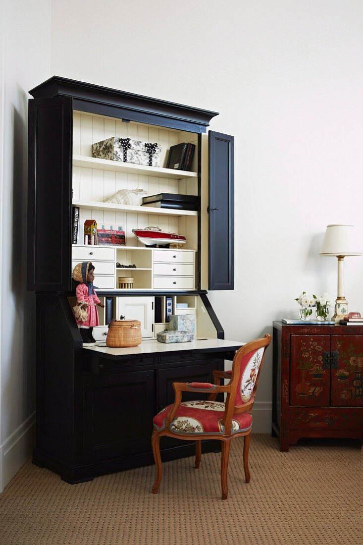 Schwarzer Schrank mit geöffneten Türen und integrierter Schreibtischplatte, davor Sessel im Rokoko Stil
