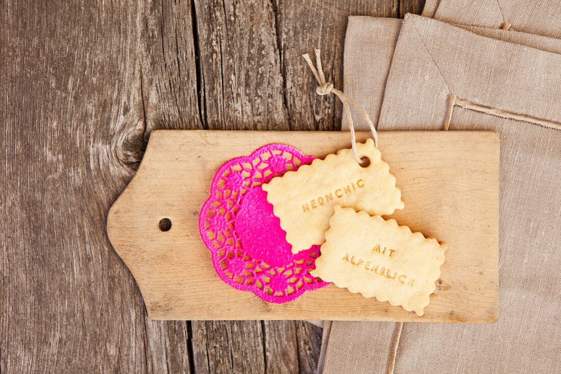 Biscuits and hot pink doily on wooden board; linen napkins on weathered wooden surface