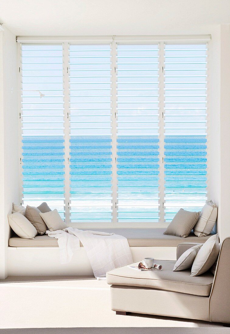 Armchairs in front of window with window seat, open glass louvres and sea view