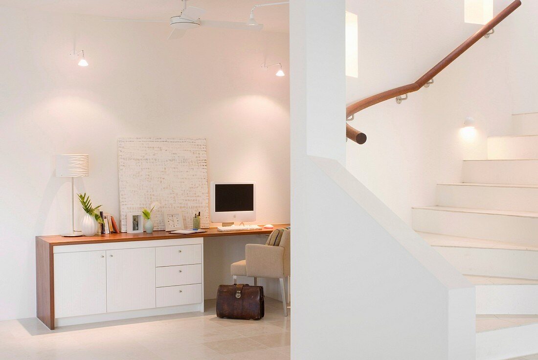 Blick von offenem Vorraum auf Arbeitsplatz, seitlich Treppenaufgang in minimalistischem Ambiente