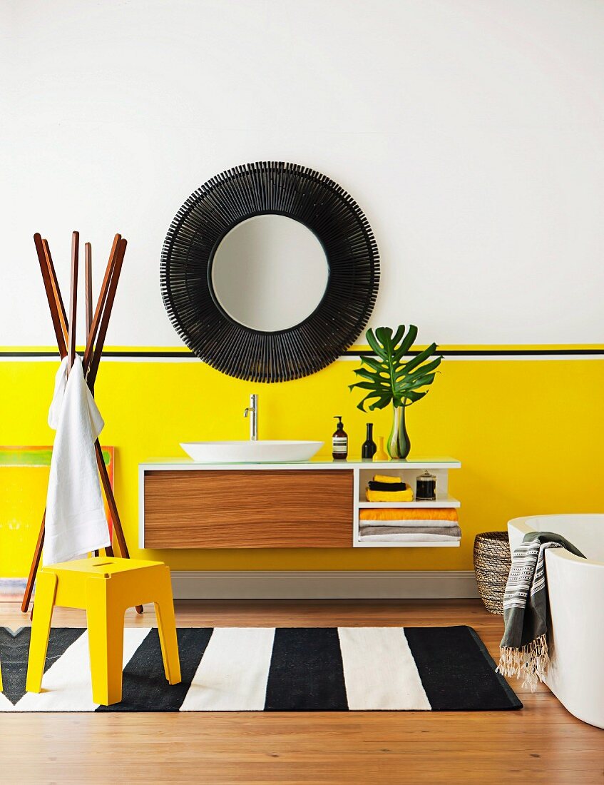 Yellow stool on black and white striped rug and floating washstand below round mirror with dark frame