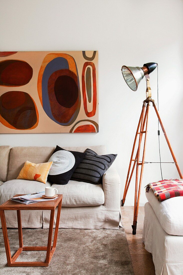 Fotoleuchte mit altem Holzstativ als Beleuchtung für Sitzgruppe mit schlichtem Coffee Table und moderner Kunst an der Wand