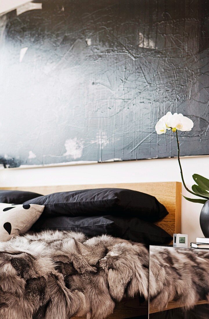 Schwarzer Kissenstapel auf Felldecke im Bett, an Wand schwarzes Gemälde