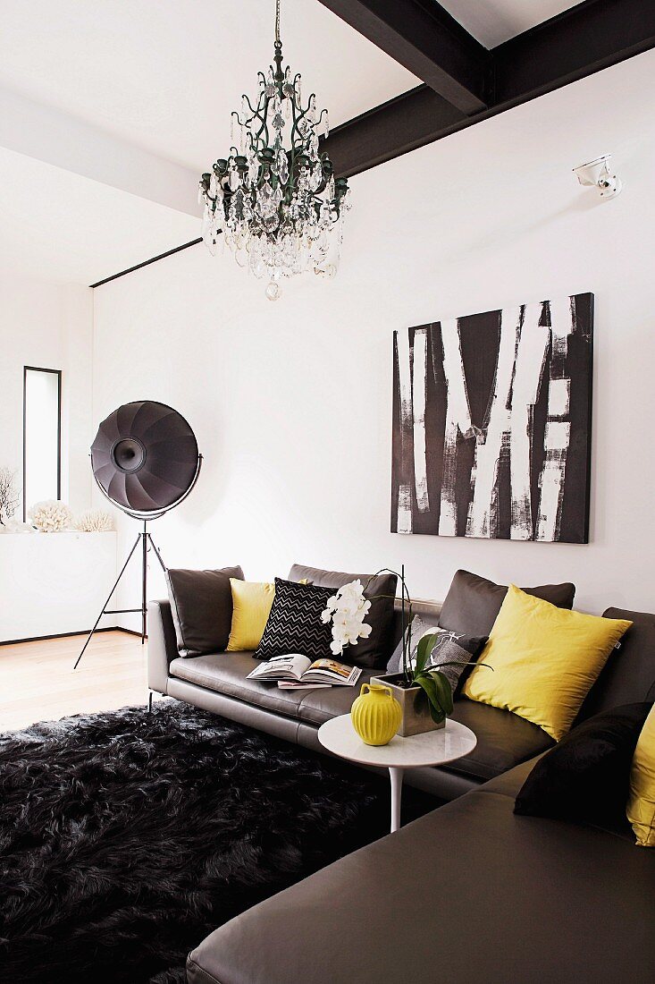 Dark grey leather corner couch on long-pile, black rug, chandelier and studio lamp in designer interior