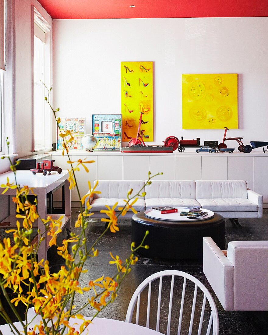 Lounge area with round coffee table and white sofa in front of wall with yellow artworks above sideboard
