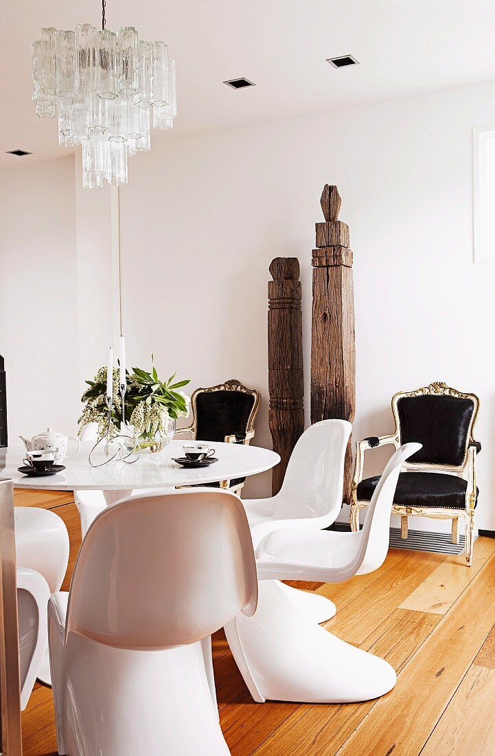 weiße Designer-Schalenstühle um Tulip Table, im Hintergrund antike Sessel mit schwarzen Polstern und antike, asiatische Holzstelen an Wand in minimalistischem Wohnraum