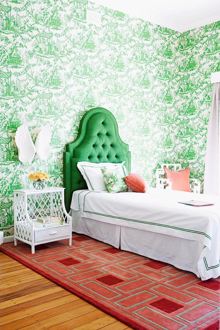 Bedroom with toile de jouy wallpaper, bed with green, upholstered headboard & red patterned rug